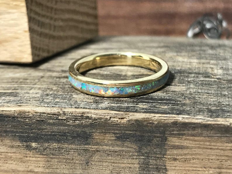 A gold ring featuring an opal inlay lies flat on a dark wooden surface.