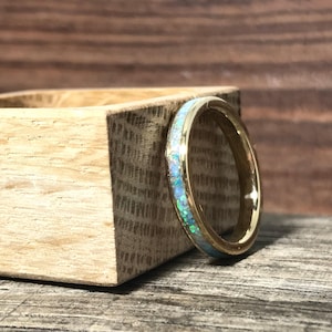 A gold ring with an opal inlay stands upright leaning against a square wooden block.