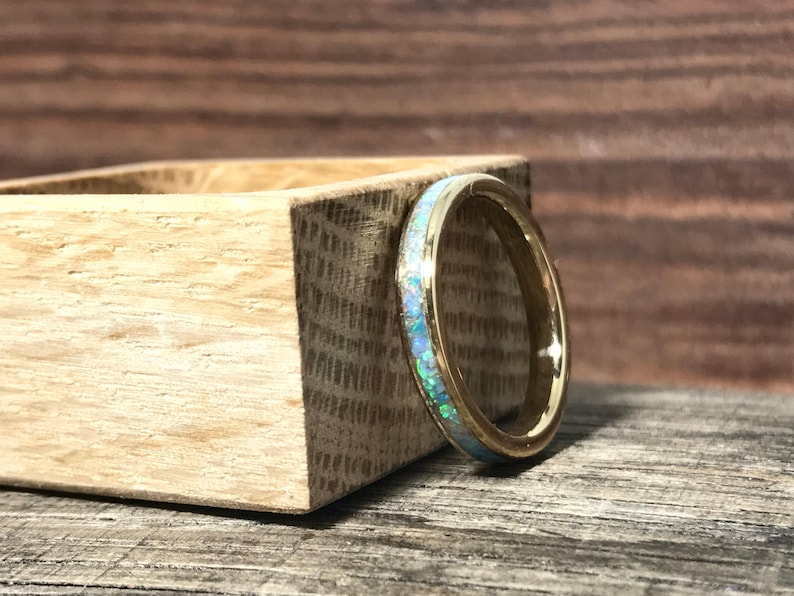 A gold ring with an opal inlay stands upright leaning against a square wooden block.