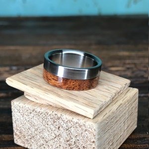 May include: A silver and wood ring with a brushed silver finish. The ring is on a wooden display stand.
