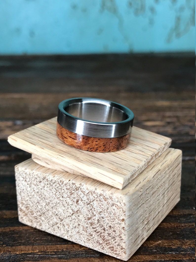 May include: A silver and wood ring with a brushed silver finish. The ring is on a wooden display stand.