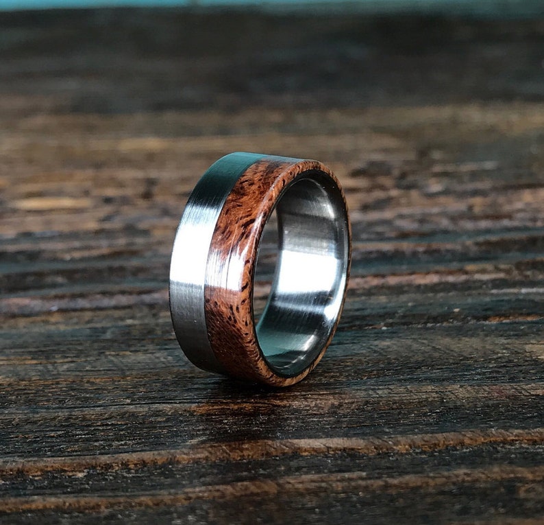 May include: A silver and brown wood ring with a polished finish. The ring is made of stainless steel and wood.
