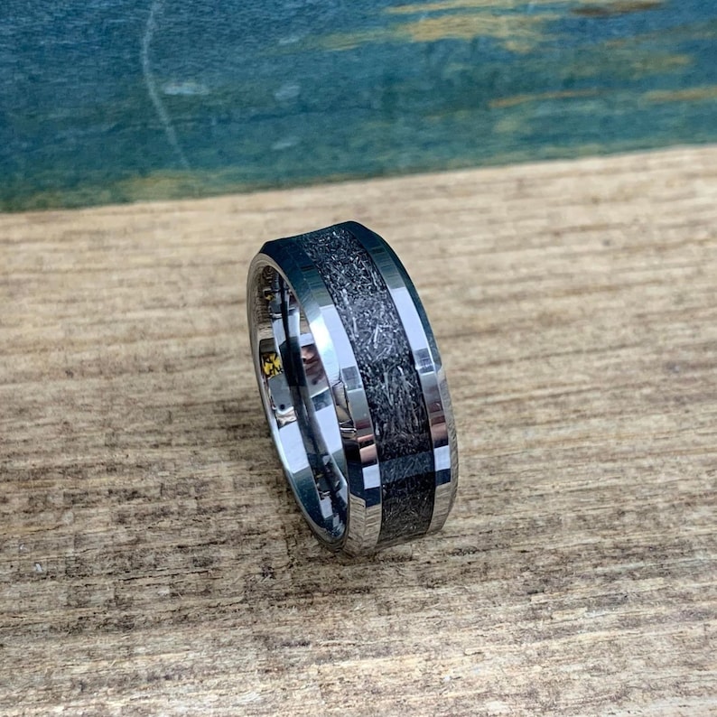 May include: A silver tungsten carbide ring with a black inlay. The inlay has a wood-like pattern.