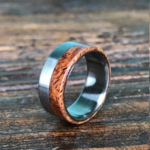 May include: A silver and wood ring with a brown wood inlay. The ring is on a wooden surface.