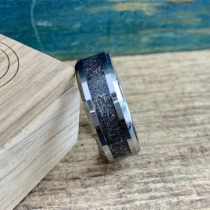 May include: A silver and black tungsten carbide ring with a beveled edge and a textured black inlay.