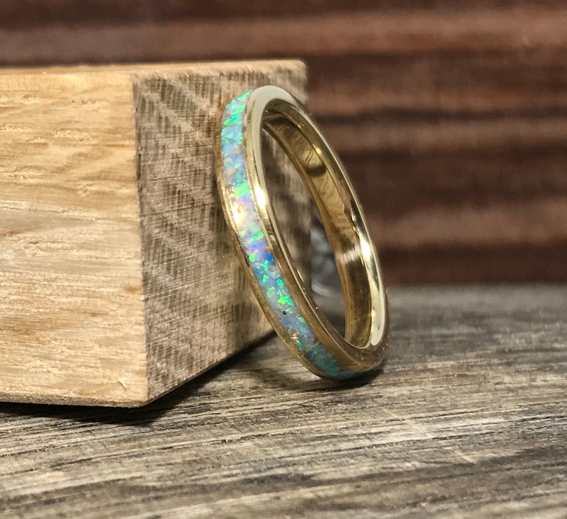 A gold ring featuring a colorful opal inlay rests vertically against a wooden block.