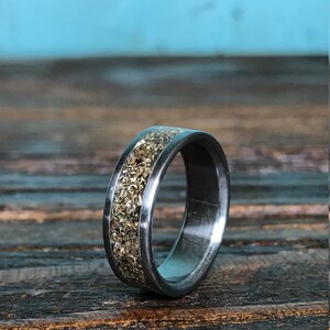 A titanium ring with a chunky gold-colored inlay resting on a rustic dark wood board with a blue backdrop.