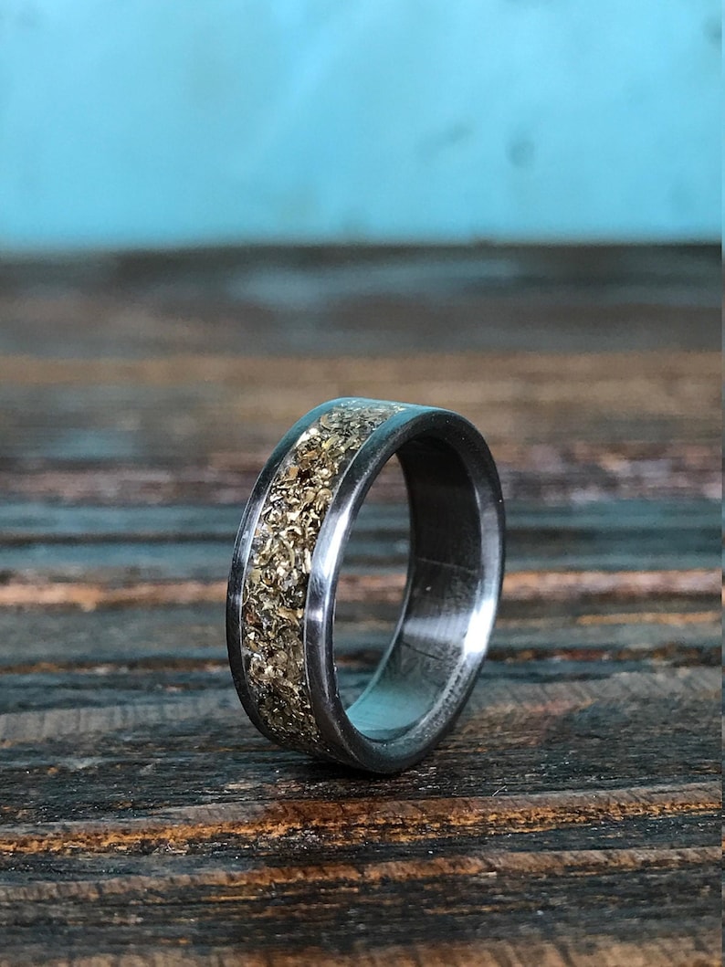 A titanium ring with a chunky gold-colored inlay resting on a rustic dark wood board with a blue backdrop.