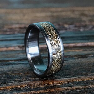 A silver-colored ring featuring a central inlay of metallic gold flakes, angled on a dark wooden surface.