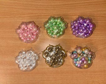 Puede incluir: Seis recipientes transparentes de plástico con forma de pata llenos de cuentas de perlas de colores. Los recipientes están dispuestos en dos filas de tres. Las cuentas son en tonos de rosa, verde, morado, blanco, dorado y multicolor.
