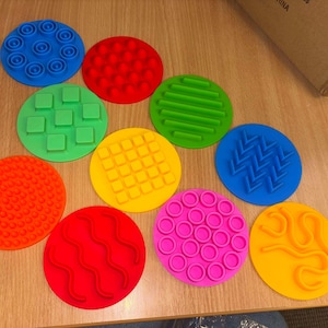 May include: Ten colourful round sensory toys with different textures, including circles, squares, and wavy lines. The toys are made of soft, pliable silicone and are perfect for tactile exploration.
