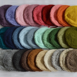 May include: A collection of 20 knitted baby bonnets in various colors, including purple, pink, red, orange, yellow, green, blue, gray, and brown. The bonnets are arranged in rows, with the colors transitioning from one row to the next.