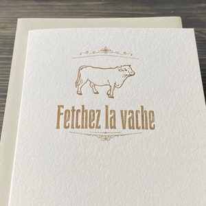 May include: A white card with a brown outline of a cow and the text "Fetch the cow" in brown lettering.