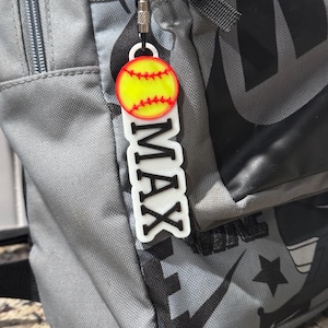 May include: A white and black personalized keychain with the name "MAX" and a yellow softball with red stitching.