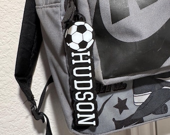 May include: Gray backpack with a black and white soccer ball keychain that says "HUDSON" in white letters.