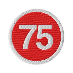 Puede incluir: Parche bordado redondo con el número 75 en blanco sobre un círculo rojo. El círculo rojo está rodeado por un borde blanco texturizado. El parche es redondo y parece ser de tela.