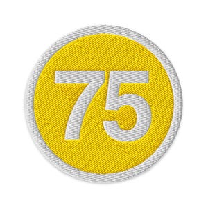 Può includere: Toppa ricamata con il numero 75 bianco su un cerchio giallo. Il cerchio giallo è incorniciato da un bordo bianco. La toppa ha un aspetto strutturato, suggerendo che sia fatta di tessuto.