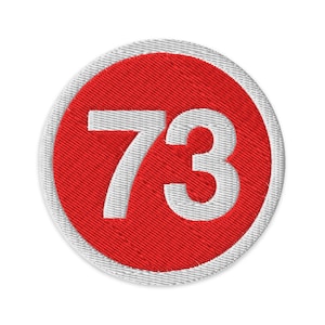 May include: Embroidered patch featuring the number 73 in white, centered on a red circle. The red circle is surrounded by a white stitched border. The patch is round and has a textured appearance.