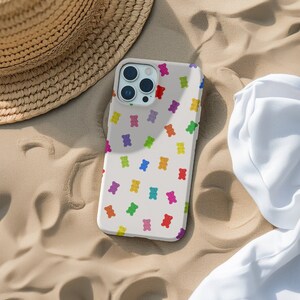 May include: A white phone case with a colourful gummy bear pattern. The case has a camera lens cutout and a white background.
