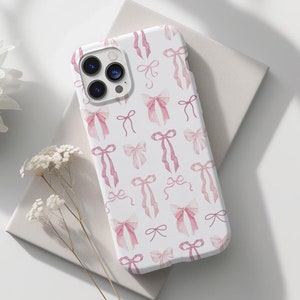May include: A white phone case with a pink watercolor bow pattern. The case is designed for an iPhone.