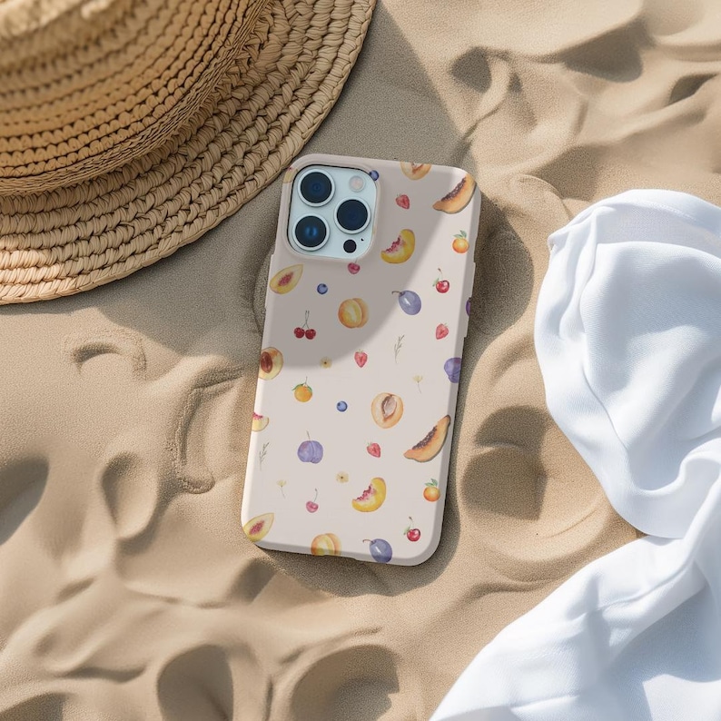 May include: A pink phone case with a pattern of peaches, plums, cherries, and blueberries. The case has a camera lens cutout and a white background.