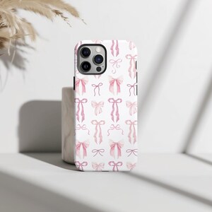 May include: A white phone case with a pink watercolor bow pattern. The case has a cutout for the camera lens.