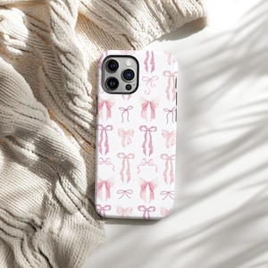 May include: A white phone case with a pink and white watercolor bow pattern. The case has a camera cutout and a white background.