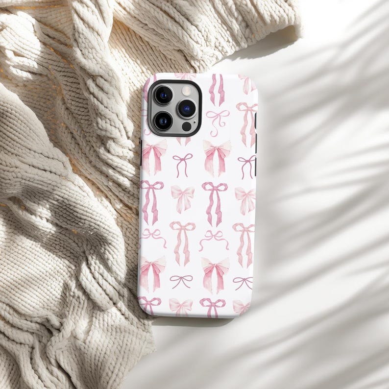 May include: A white phone case with a pink and white watercolor bow pattern. The case has a camera cutout and a white background.