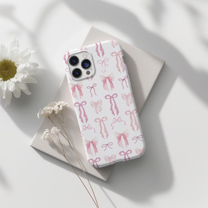 May include: A white phone case with a pink watercolor bow pattern. The case is designed for an iPhone.