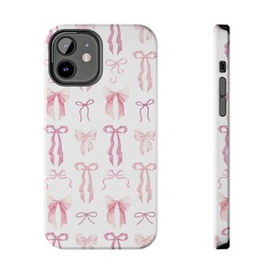 May include: A white phone case with a pink watercolor bow pattern. The case is designed for a smartphone with a camera bump.
