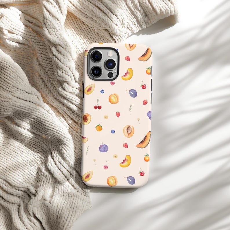 May include: A white phone case with a pattern of peaches, plums, cherries, and strawberries on a light pink background.