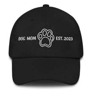 Può includere: Cappellino da baseball nero con ricamo bianco che recita "Dog Mom" con un'impronta di zampa al centro e "Est. 2023" a destra.