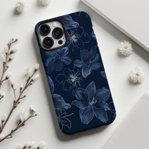 Puede incluir: Una funda para smartphone de color azul marino oscuro con un patrón repetitivo de lirios dibujados con líneas blancas y azul claro. La funda tiene un recorte para un sistema de cámara de triple lente en la parte posterior con diseño floral.