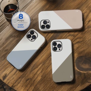 May include: Three different phone cases with a white background and a diagonal colour stripe. The cases are all matte and have a camera cutout. The colours are blue, beige, and grey.