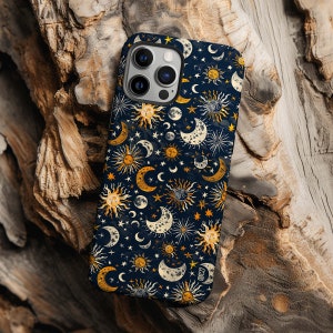 May include: A navy blue phone case featuring a celestial pattern of suns, moons, and stars in shades of gold, white, and yellow. The case is designed to fit a smartphone and has a glossy finish. The case is resting on a piece of wood.