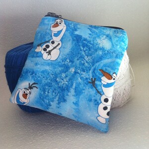 Puede incluir: Una bolsa azul con cremallera con un patrón repetido de Olaf el muñeco de nieve de la película Frozen. La bolsa está hecha de tela y tiene un fondo blanco con copos de nieve azules.