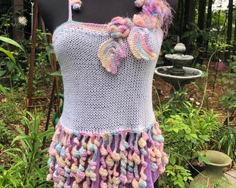 May include: White crochet top with a pink, blue, and yellow flower design. The top has a crocheted fringe around the bottom.