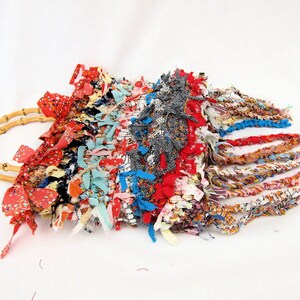 May include: A colorful woven bag with a bamboo handle and fringe details. The bag is made from a variety of fabrics in shades of red, blue, yellow, and green.