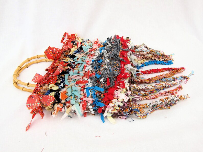 May include: A colorful woven bag with a bamboo handle and fringe details. The bag is made from a variety of fabrics in shades of red, blue, yellow, and green.