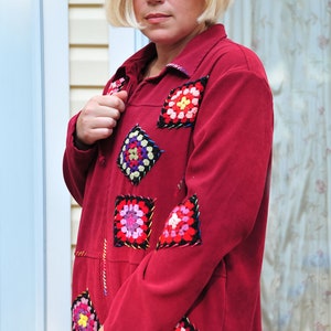 May include: A red jacket with colorful crocheted squares sewn on the front and sleeves. The jacket has a collar and long sleeves. The person wearing the jacket is wearing sunglasses.