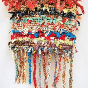 May include: A colorful woven bag with a fringe made of fabric scraps. The bag has a red, blue, and white color scheme and is made with a variety of different fabrics.