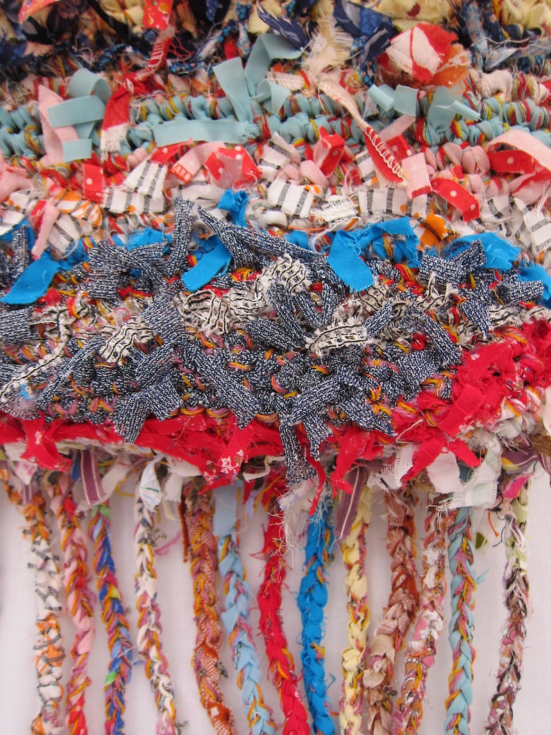 May include: A colorful woven rug with a fringe made of various fabrics, including denim, red, blue, and white. The rug is made with a variety of textures and patterns.