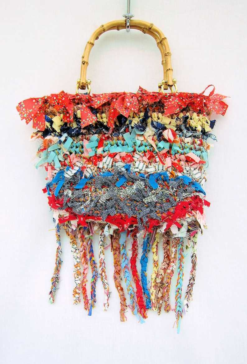 May include: A colorful woven handbag with a bamboo handle and fringe details. The bag is made from a variety of fabrics in shades of red, blue, yellow, and white.