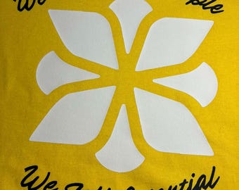 May include: Yellow t-shirt with the text "We Don't Sell People, We Sell Potential" in black script. A large white floral design is centered on the shirt. The shirt is made of a soft material.