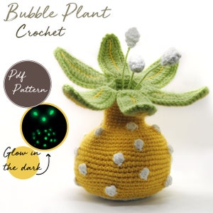Pode incluir: Uma planta de bolhas de crochê com uma base amarela e bolinhas brancas. A planta tem folhas verdes e flores brancas. A base brilha no escuro. Padrão PDF incluído.