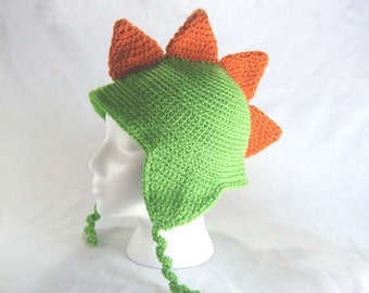 May include: Green and orange crocheted dinosaur hat with ear flaps and a long tail.