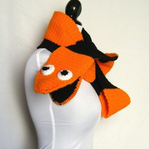 May include: A crocheted scarf with an orange and black striped pattern. The scarf has a crocheted fish face with white eyes and a black mouth.