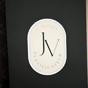 May include: Black journal with a white oval sticker that says "L'Agenda JV Planificateur" and "a Writer's Journal" in gold lettering.