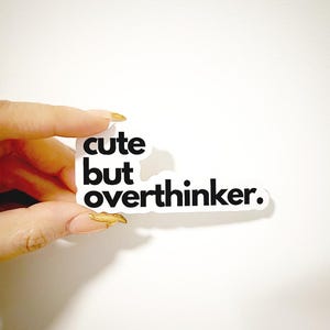 Peut inclure: Autocollant blanc avec du texte noir qui dit "cute but overthinker."