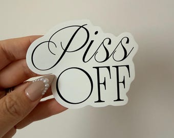May include: A white sticker with the words "Piss OFF" in black script. The sticker has a unique shape with a circular design element. The text is in a bold, easy-to-read font.